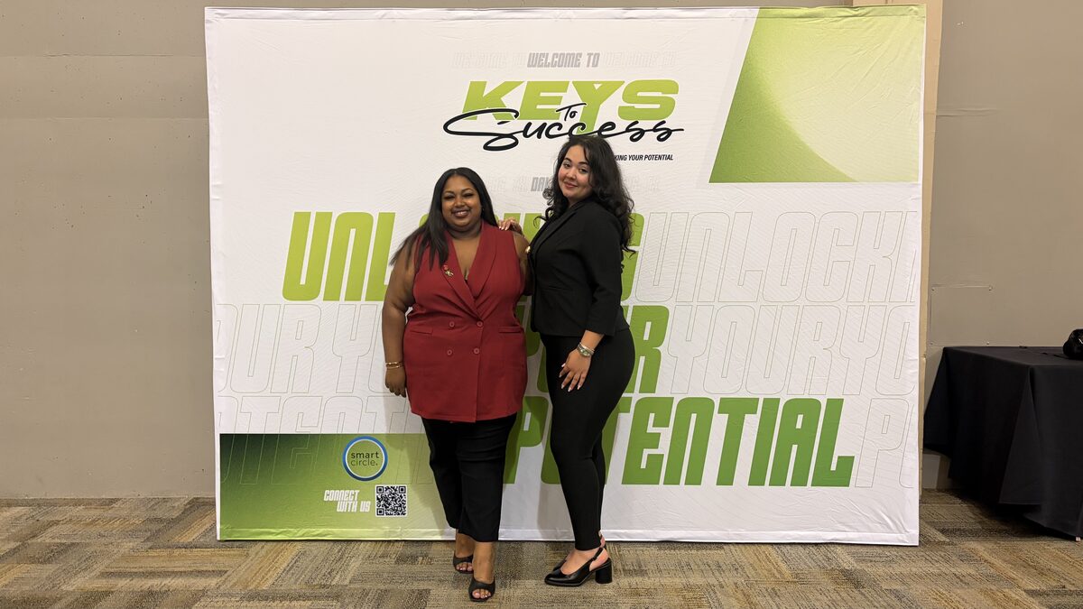 Two ALL-IN Marketing team members in front of a Keys to Success backdrop reading Unlocking Your Potential